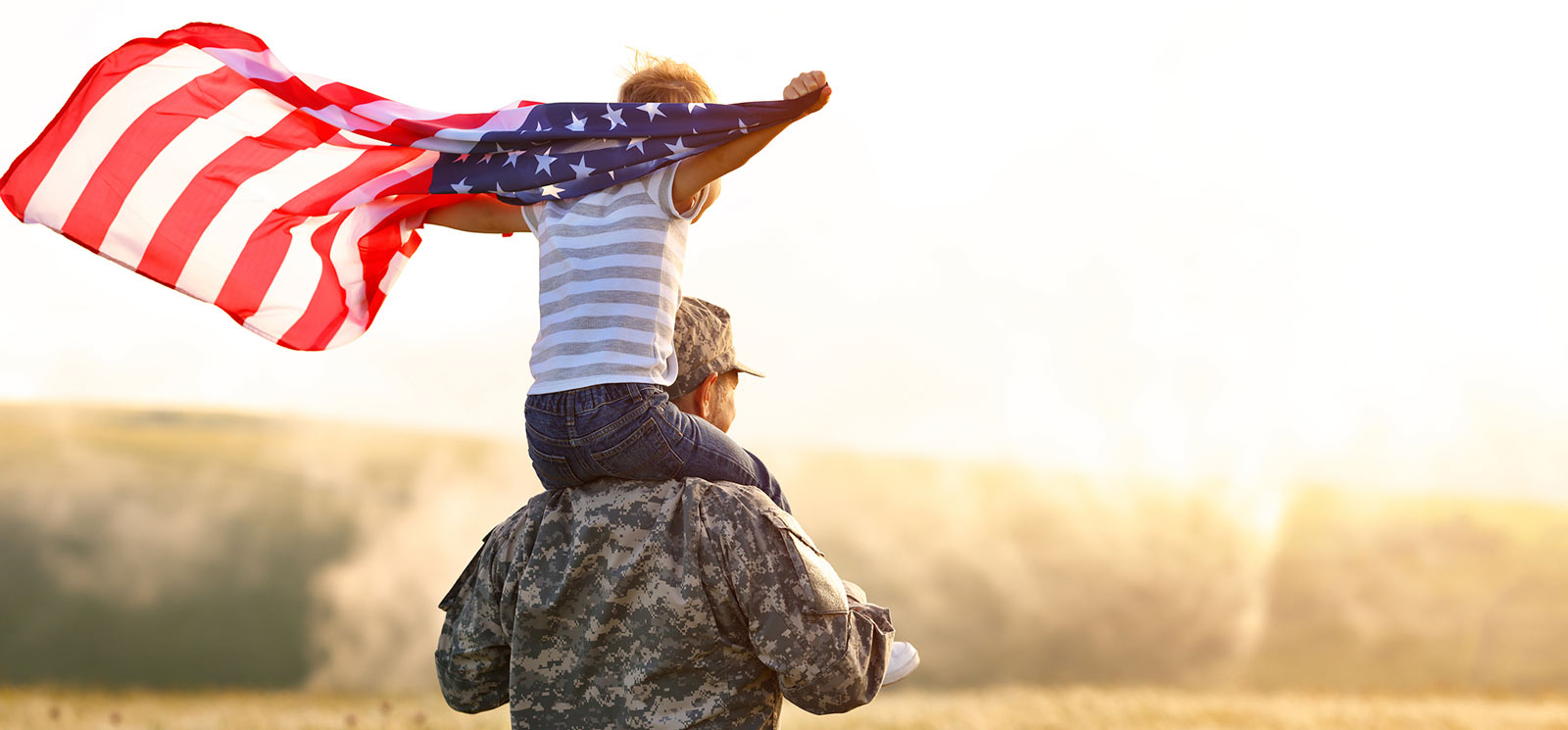 Child holding American flag sitting on his father's shoulders.